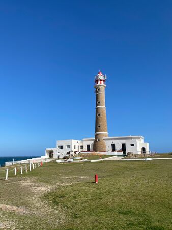 Cabo Polonios Wahrzeichen, der weiß-graue Leuchtturm vor tiefblauem Himmel. Im Vordergrund eine grüne Rasenfläche.