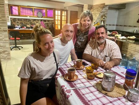 4 Erwachsene, die sich an einem Tisch mit karierter Tischdecke Und Kaffee darauf in einem Haus in Argentinien befinden. Alle lächeln freundlich in die Kamera.