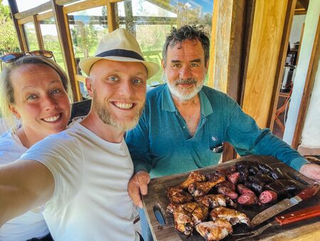 Ein Selfie von zwei Europäern mit einem Argentinier, der ein traditionelles argentinisches Asado serviert. Alle sehen sehr glücklich aus. Das perfekte Erinnerungsfoto an eine tolle Begegnung.