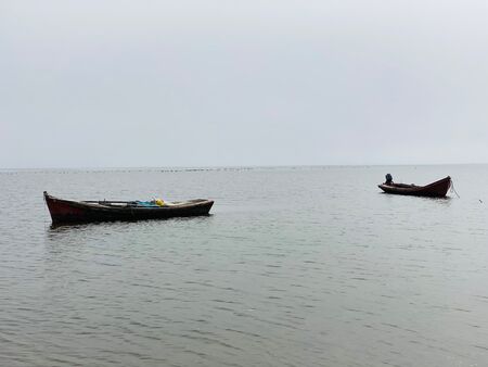 Zwei Boote, die auf friedlichem Wasser liegen. Der Himmel ist grau, das Wasser strahlt.