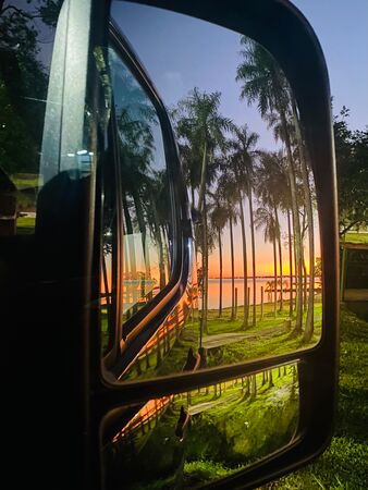 Der Rückspiegel eines Vans in dem hohe Palmen und ein wahnsinnig schöner Sonnenuntergang zu sehen sind. Aufgenommen am Rio Paraná in Argentinien.