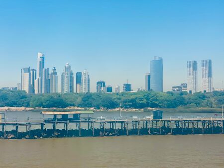 Blick auf die Skyline von Buenos Aires vom Wasser aus. Das Bild wirkt milchig, da es durch eine Scheibe einer Autofähre aufgenommen wurde. Im Vordergrund der bräunliche Rio de la Plata. Im Hintergrund die Wolkenkratzer von Buenos Aires.