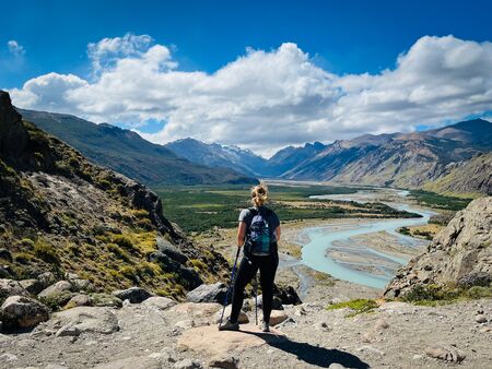 Eine Frau von hinten in Outdoorkleidung, die auf ein wunderschönes Flusstal, welches ein bisschen wie im Auenland aussieht, schaut. Aufgenommen auf dem Sendero al Fitz Roy in El Chaltén.