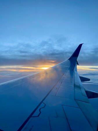 Der Flügel eines Flugzeugs aus dem Passagierfenster heraus fotografiert. Es ist spät am Abend und die Sonne geht unter. Das besondere blau-goldene Licht spiegelt sich im Flügel des Flugzeugs.
