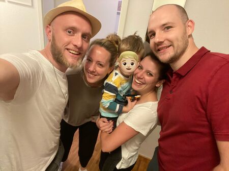 Ein Selfie von vier Erwachsenen (2 Frauen und 2 Männer) und einem kleinen Kind, welches von der einen Frau auf dem Arm gehalten wird. Alle sehen glücklich aus.