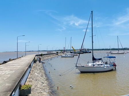 Segelboote liegen im Puerto de Yates in Colonia del Sacramento, Uruguay, mit einem langen Steg, der zu ihnen führt. Die Szene zeigt die malerische Atmosphäre des Yachthafens, umgeben von ruhigem Wasser.