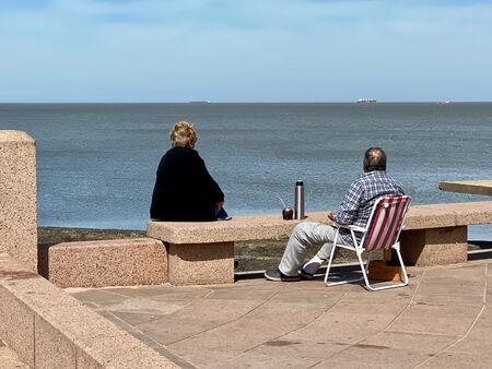 Ein entspanntes Ehepaar sitzt am Strand von Uruguay und genießt gemeinsam Mate Tee. Sie schauen auf das ruhige Meer und lassen sich von der malerischen Szenerie verzaubern.
