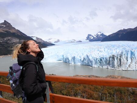 Eine Frau steht auf einer Aussichtsplattform und genießt die Aussicht auf den majestätischen Perito Moreno Gletscher in Patagonien, Argentinien. Im Hintergrund sind der riesige Gletscher und die umliegenden Berge zu sehen.