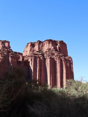 Eine besondere Felsformation im Talampaya-Nationalpark in Argentinien. Der Himmel ist strahlend blau, im Vordergrund ist schattiges Grün und die Felsformation leuchtet rot (Sandstein).