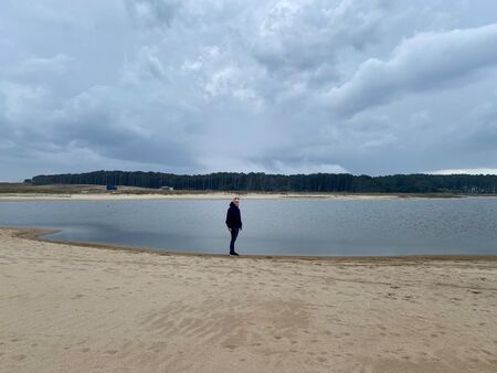 Ein Mann steht bei bewölktem Wetter an der Laguna de Rocha in Uruguay. Im Vordergrund Sand, im Hintergrund Wasser und Bäume.