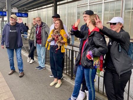 Eine kleine Gruppe von Menschen steht am Bahnhof und winkt.