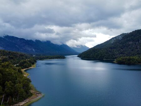 Ein dunkelblauer See umgeben von baumbewachsenen grünen Bergen. Der Himmel ist bewölkt, die Aussicht trotzdem fantastisch. Der See befindet sich entlang der 7 Seen Route in Argentinien.