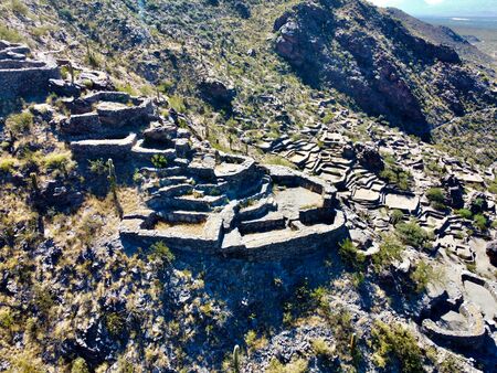 Luftaufnahme der Quilmes-Ruinen auf einem felsigen Wüstenhügel in Argentinien, umgeben von Kakteen und spärlicher Vegetation bei klarem Sonnenlicht.