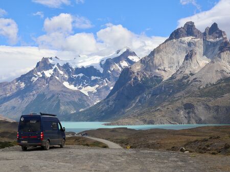 Ein blauer Van vor einem türkisfarbenem See von dem aus direkt die unverwechselbaren Berge des Torres del Paine Nationalparks in die Höhe ragen. Es ist leicht bewölkt, doch der Himmel strahlt trotzdem blau auf die wahnsinnig beeindruckende Bergwelt hinab.