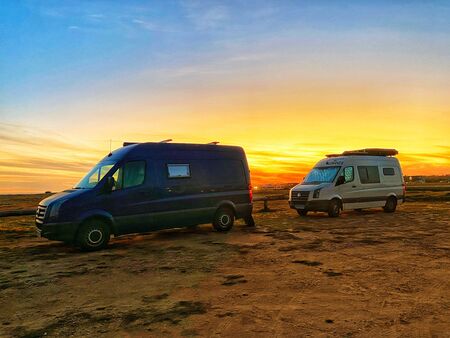 Zwei VW Crafter (ein blauer und ein weißer) stehen hintereinander. Man sieht sie von der Seite und im Hintergrund einen fantastischen Sonnenuntergang.
