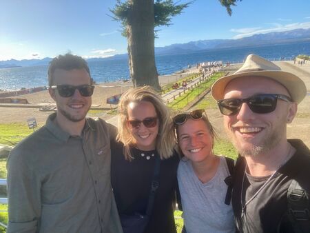Ein Selfie von vier jungen Erwachsenen, die in Bariloche sind. Weit im Hintergrund der tiefblaue See und das Bergpanorama der Anden.