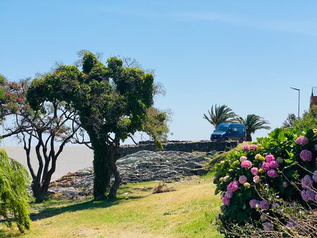 Die idyllische Gartenanlage des Mirador al Río in Colonia del Sacramento, Uruguay, bietet eine malerische Kulisse mit blühenden Blumen und gepflegten Grünflächen. Im Hintergrund steht unser blauer VW Crafter Wohnmobil, bereit für weitere Abenteuer.