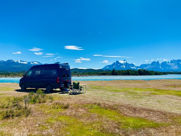 Ein Reisender steht auf einem Fels in einem türkisblauen See und schaut in die Ferne. Umliegend ein atemberaubendes Bergpanorama. Aufgenommen ist das Foto im Parque Nacional Tierra del Fuego.