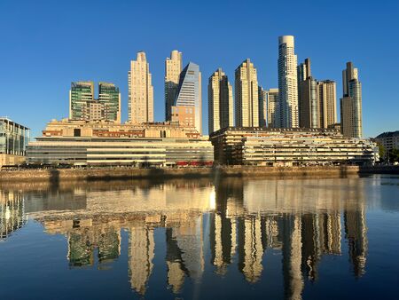 Die Skyline von Buenos Aires im Abendlicht. Die Wolkenkratzer spiegeln sich im Wasser des Hafenbeckens.