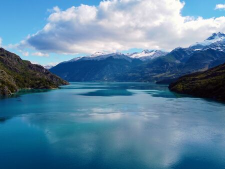 Ein Panoramablick auf den Lago Bertrand, der von den majestätischen, schneebedeckten Bergen der Carretera Austral in Chile umgeben ist. Der See strahlt in einem atemberaubenden Blau, das die umliegenden, dicht bewaldeten Hänge spiegelt.
