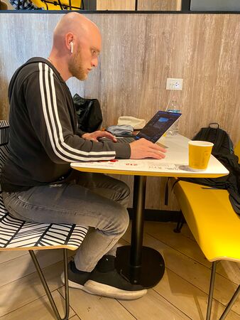 Ein junger Mann mit Glatze sitzt in einem McDonalds und arbeitet am neuen YouTube-Video