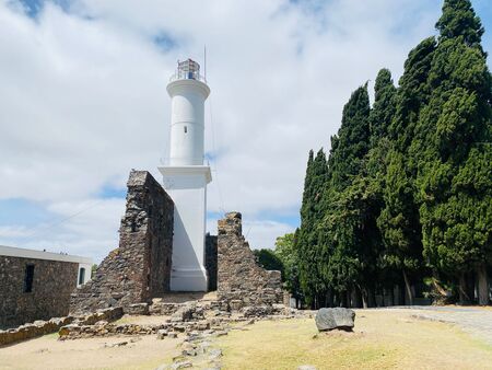 Der historische Faro de Colonia del Sacramento steht majestätisch vor dem Himmel. Sein weißer Turm hebt sich von den umliegenden Bäumen ab. Dieser Leuchtturm aus dem 19. Jahrhundert ist ein Symbol der maritimen Geschichte Uruguays.