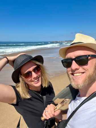 Ein Selfie eines jungen Ehepaares am Strand in Uruguay. Beide tragen einen Sonnenhut und eine Sonnenbrille. Sie sehen glücklich aus und der Himmel ist strahlend blau.