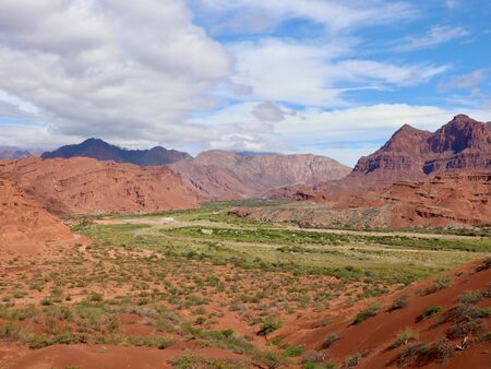 Berglandschaft mit roten Felsformationen und einem grünen Tal unter einem teilweise bewölkten Himmel entlang der Ruta 68 in Argentinien.