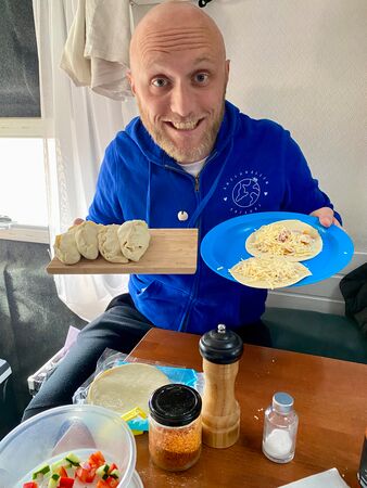 Ein Mann hält halbfertige und fertig gefaltete Empanadas in die Kamera. Sein Blick ist voller Vorfreude auf das leckere Mal. Die Empanadas müssen nur noch gebacken werden.