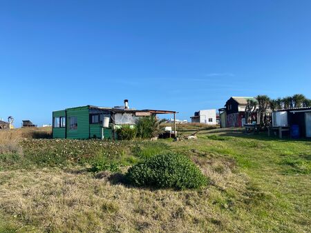 Ein grünes Tiny House auf grüner Wiese in Cabo Polonio, Uruguay. Keine Menschenseele ist zu sehen. Im Hintergrund andere Häuschen. Der Himmel ist tief blau.